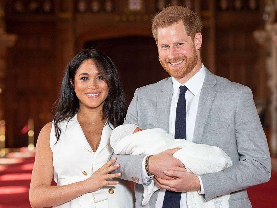 Prince Harry and Meghan Markle holding their newborn baby in a formal indoor setting. — Meghan Markle Background