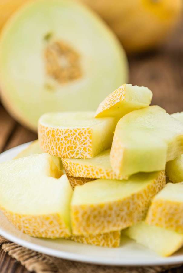 Rodajas de fruta cantalupo en un plato blanco con un melón partido por la mitad al fondo. — Melón Honeydew Fondos de pantalla