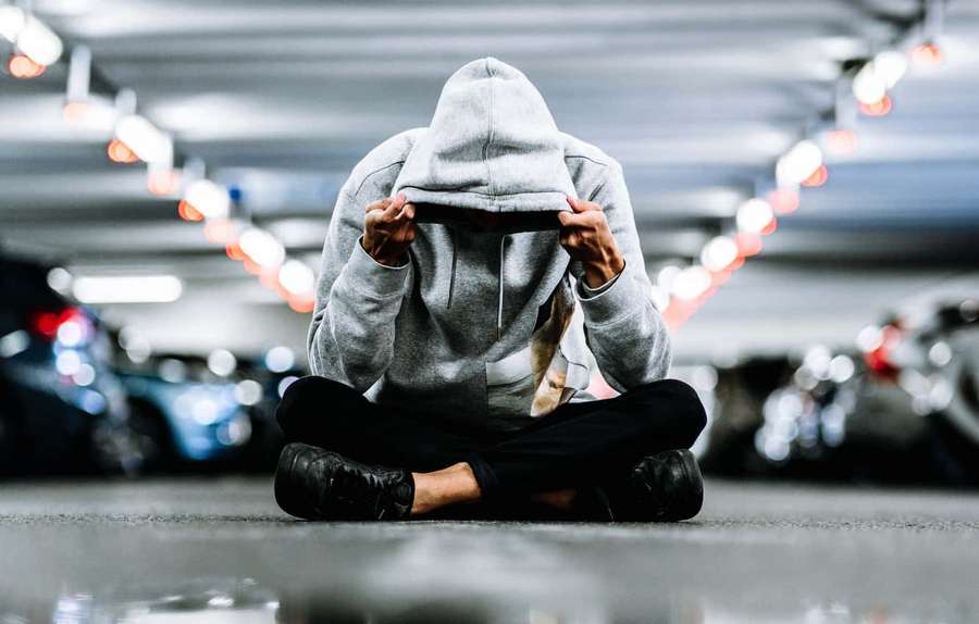 A person in a grey hoodie sits on a parking garage floor holding their head. — Men Background