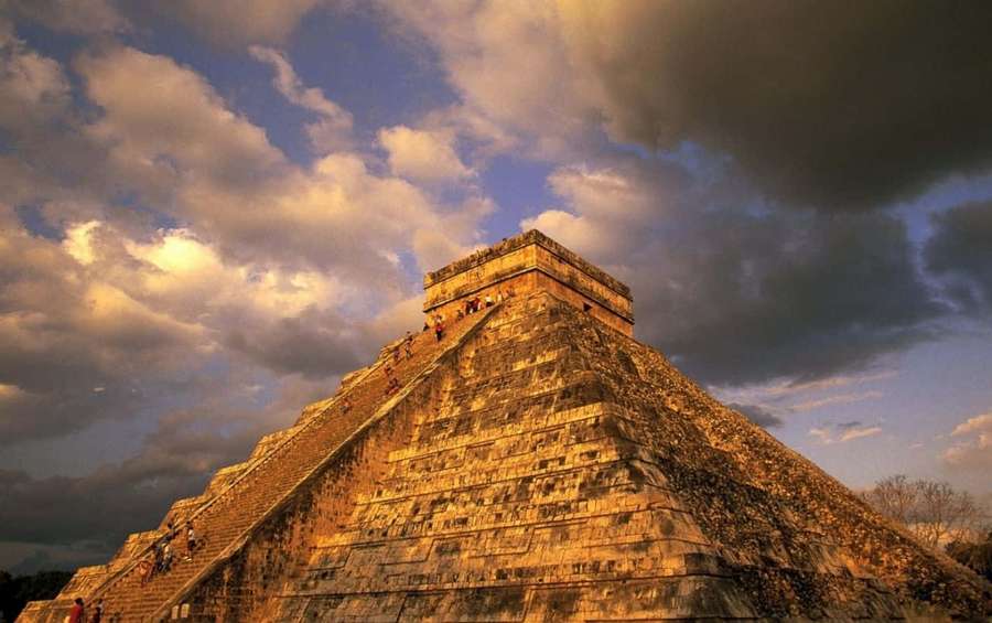 Mayan pyramid at golden hour with visitors climbing under dramatic clouds. — Mexico Background
