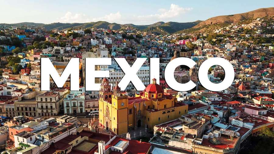 Aerial photo of a colorful Mexican town with a yellow church and mountains in the background. — Mexico Picture