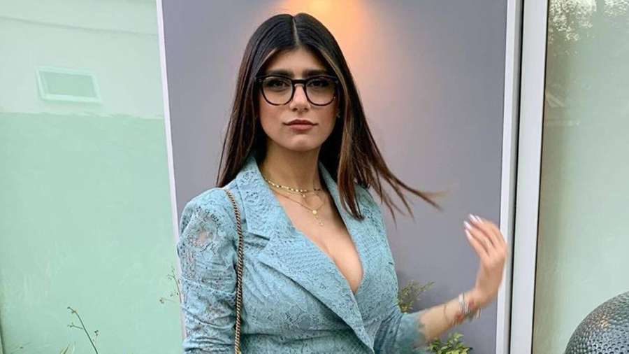 Woman in blue lace blazer and glasses standing near glass door — Mia Khalifa Background
