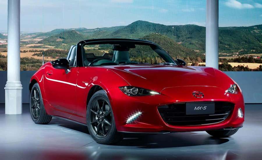 Red Mazda MX-5 Miata convertible on display with mountain backdrop. — Miata Background
