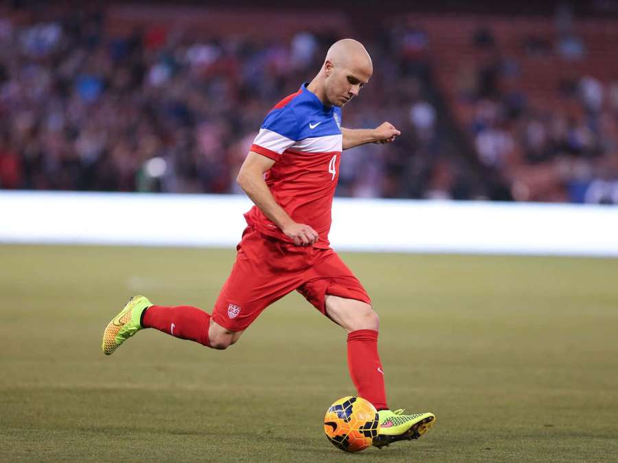 Soccer player dribbling ball on grass field at night under stadium lights. — Michael Bradley Wallpaper