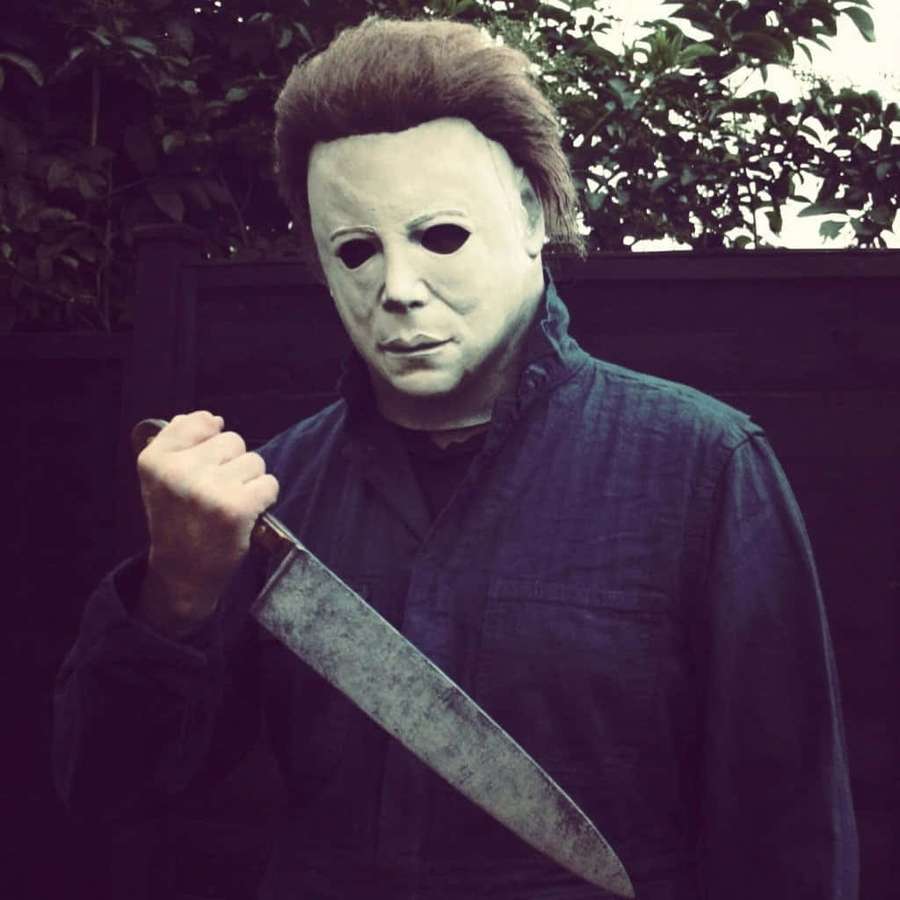 Person in white mask holding large knife outdoors near foliage. — Michael Myers Picture