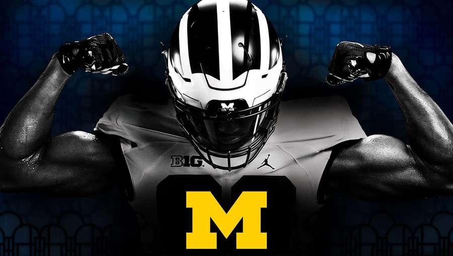 Football player flexing in Michigan uniform with yellow M logo. — Michigan Football Background