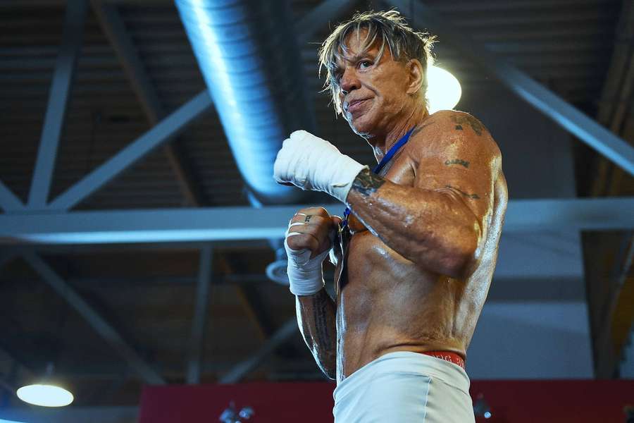 A muscular boxer in white gloves and trunks stands ready in a gym. — Mickey Rourke Wallpaper