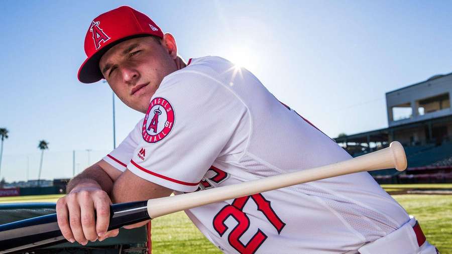 Baseball player in Angels uniform leaning on bat at sunny stadium. — Mike Trout Wallpaper