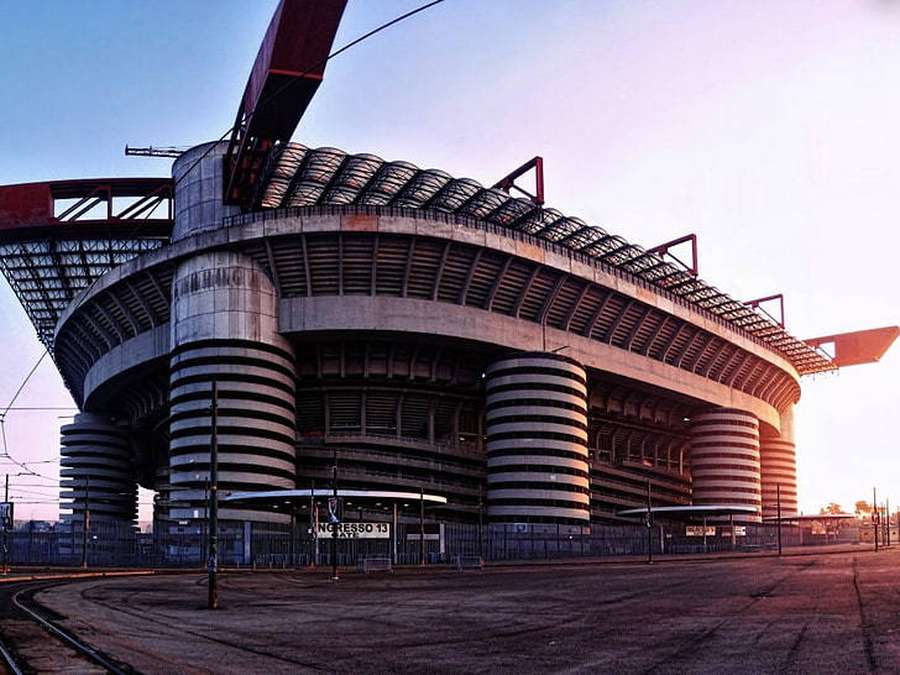 Large unfinished concrete stadium at sunset with empty stands and railway tracks. — Milan Wallpaper