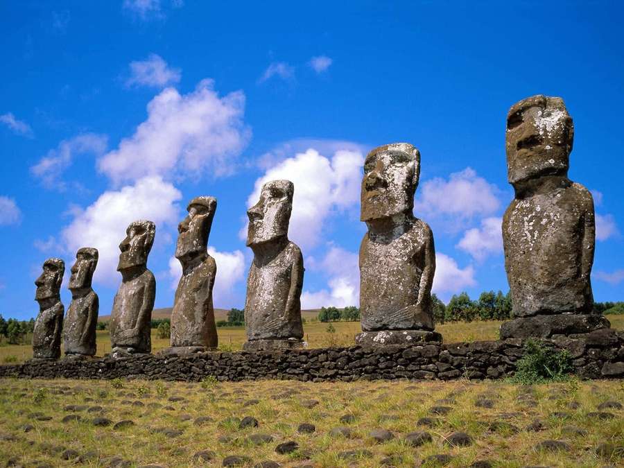 Line of giant stone moai statues under bright blue sky with clouds. — Moai Wallpaper
