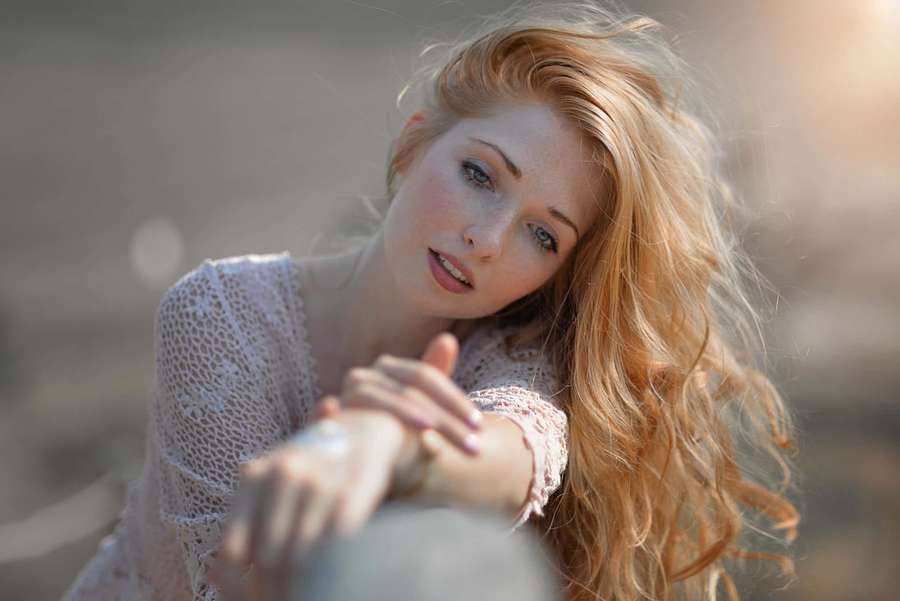 A woman with red hair and blue eyes leans on a stone in golden sunlight. — Model Picture