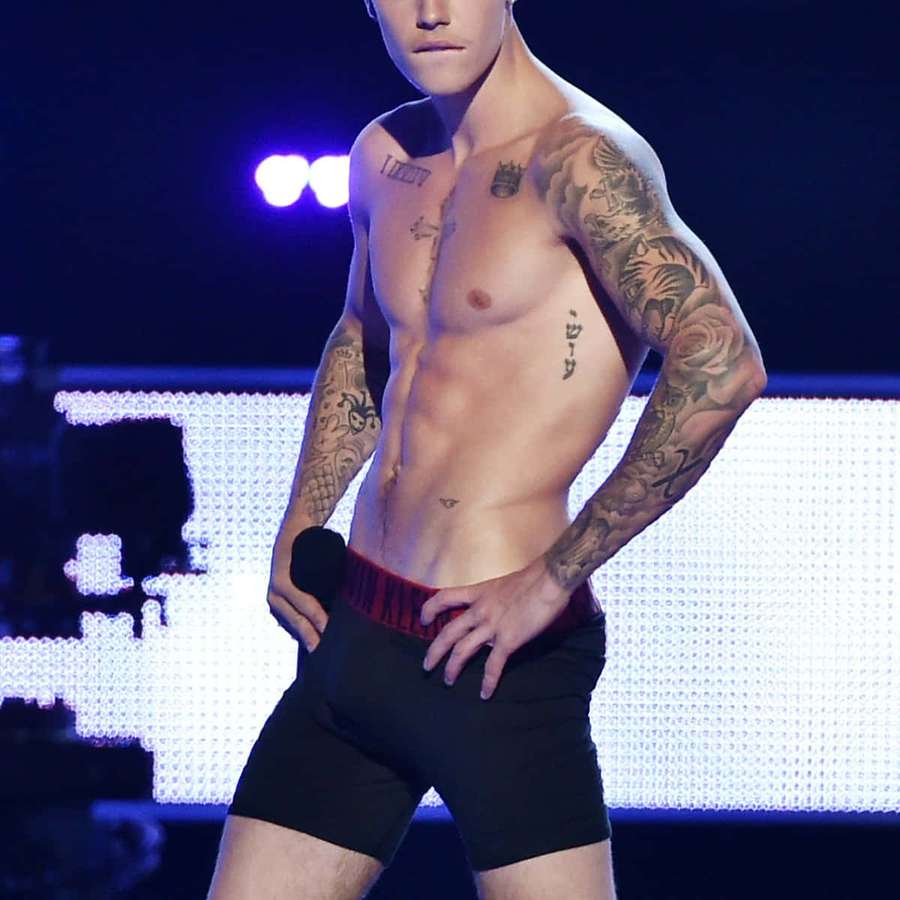 Hombre musculoso tatuado posando en el escenario en ropa interior negra bajo luces moradas. — Modelo sexy Fondos de pantalla