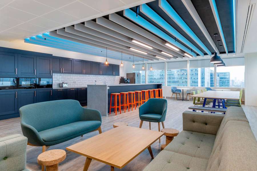 Moderne Bürolounge mit türkisfarbenen Sofas, Holztischen und orangefarbenen Hockern mit Blick auf die Stadtsilhouette. — Moderne Ästhetik Wallpaper