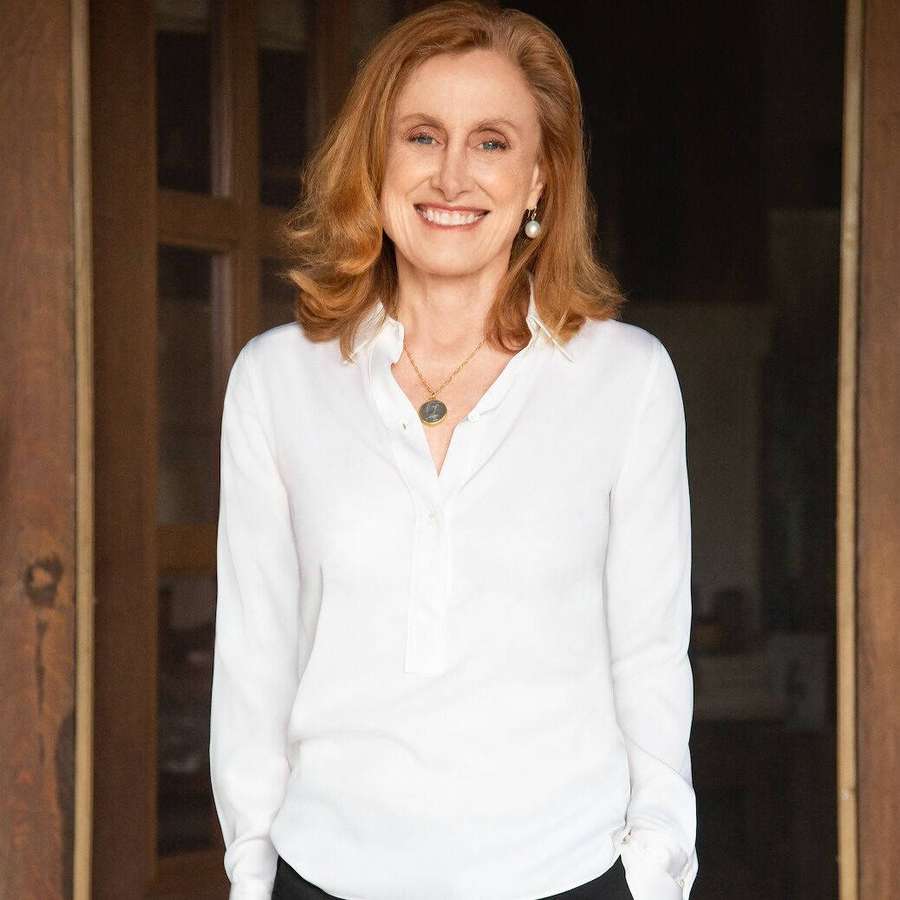 A woman with red hair smiles warmly in a wooden doorway wearing a white blouse. — Mona Simpson Wallpaper