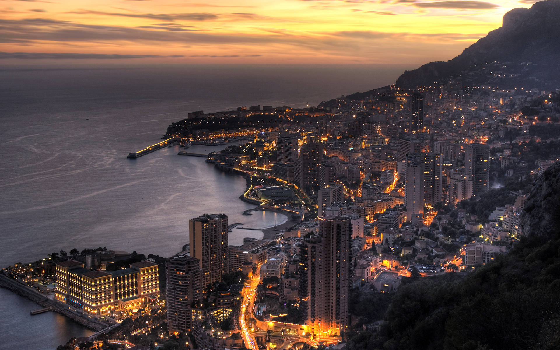 Monaco stadsbild i skymningen med glödande ljus längs kusten och bergssidan. — Monaco Bilder