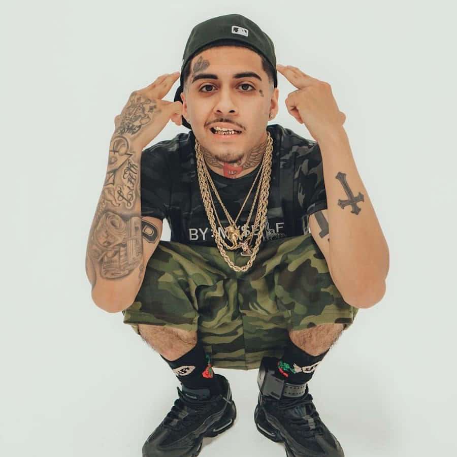 Tattooed man in camo shorts and cap posing with hands on temples. — Moneysign Suede Wallpaper