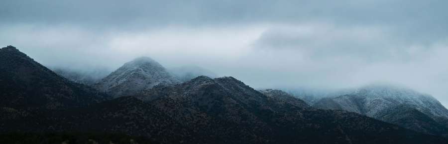 Montanhas cobertas de neve parcialmente escondidas pela névoa sob um céu cinzento. — Monitor Space Dual Papéis de Parede