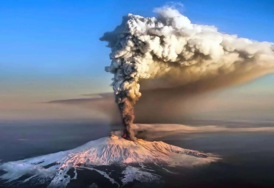Un vulcano innevato erutta con un imponente pennacchio di cenere durante l'alba. — Monte Etna Sfondi
