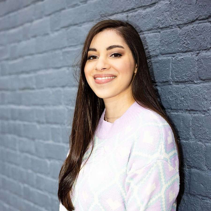 Young woman smiling in a pastel sweater against a gray brick wall. — Moriah Elizabeth Wallpaper
