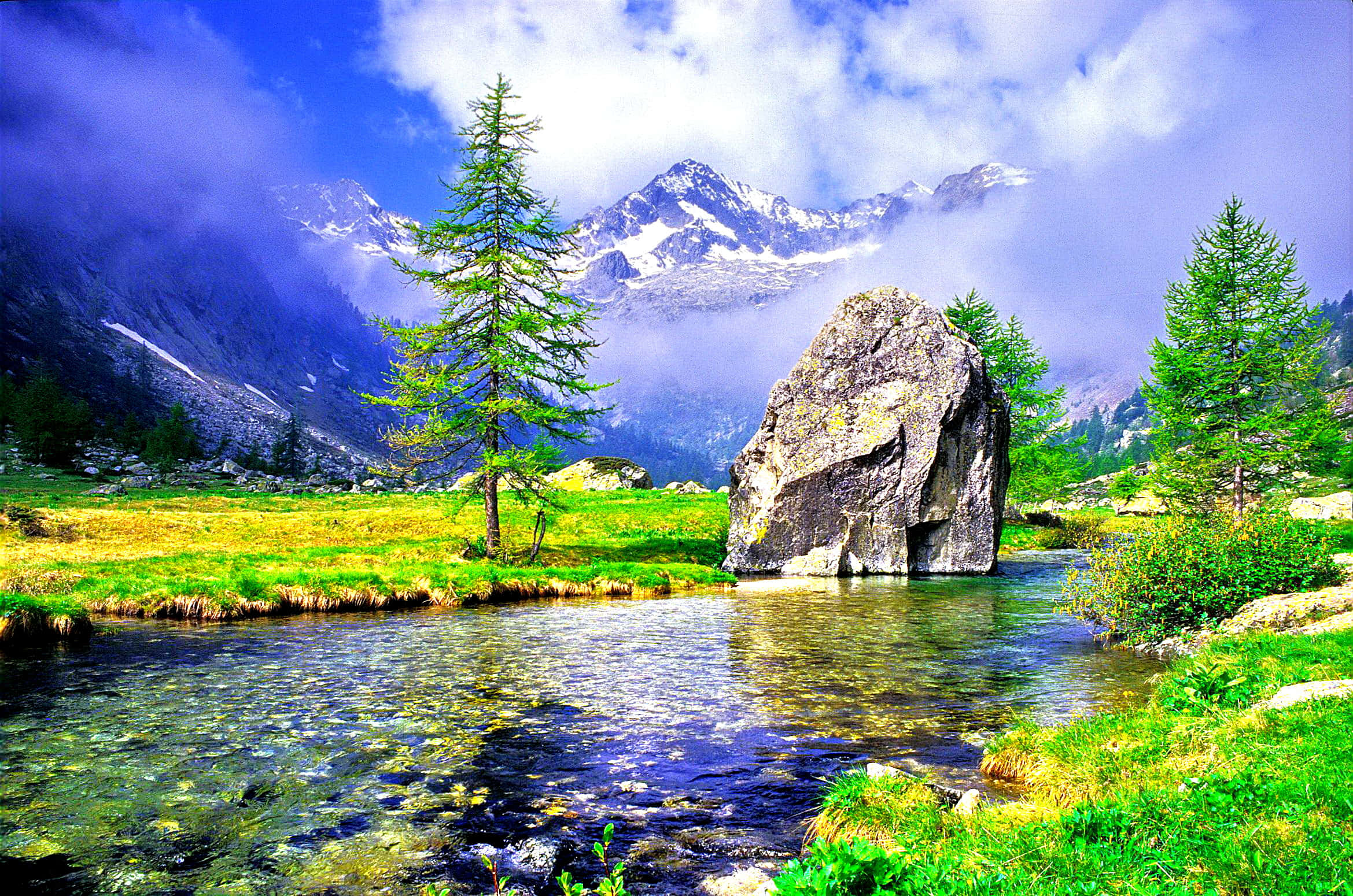 A scenic mountain valley with a stream, boulder, and evergreen trees under a cloudy sky. — Most Beautiful Nature Wallpaper