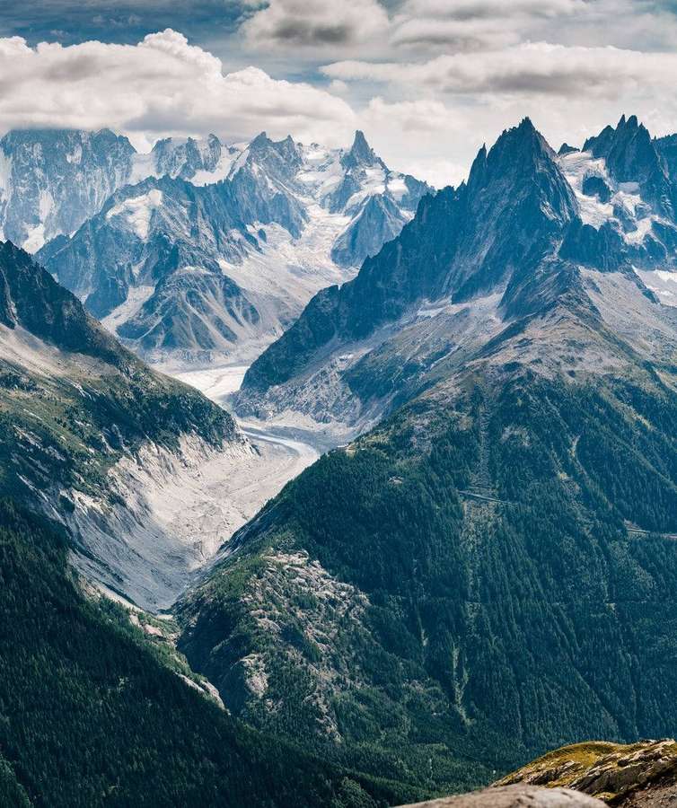 Snow-capped mountains with a glacier flowing through a forested valley. — Mountains Picture