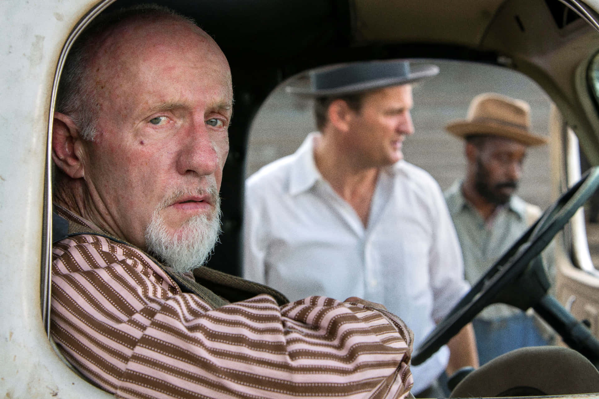 Ein älterer Mann mit weißem Bart sitzt in einem Oldtimer, während zwei Männer draußen stehen. — Mudbound Wallpaper