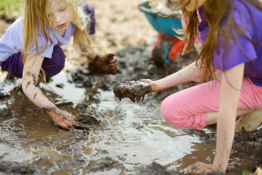 Two children playing in a muddy puddle outdoors. — Muddy Waters Background