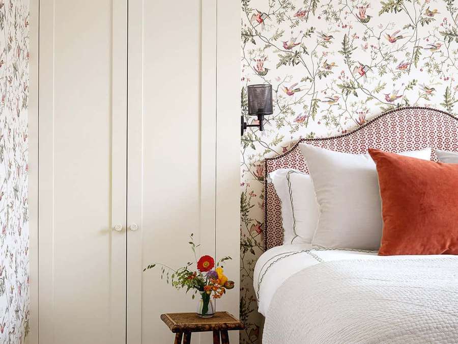 Cama con ropa blanca y almohada naranja contra papel tapiz floral con pájaros y vegetación. — Muebles Fondos de pantalla
