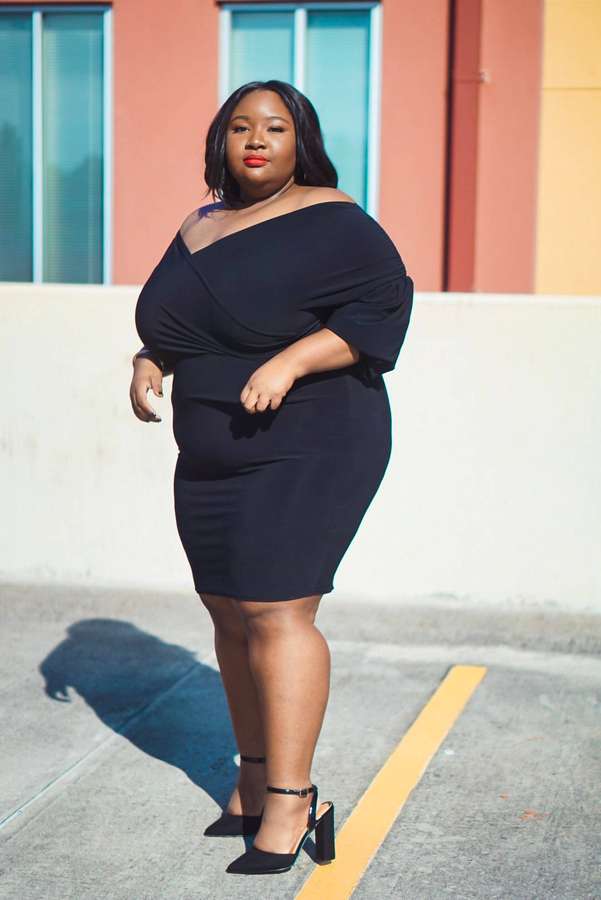 Mujer de talla grande con vestido negro y tacones parada en la acera cerca de un edificio colorido. — Mujer negra Fondos de pantalla