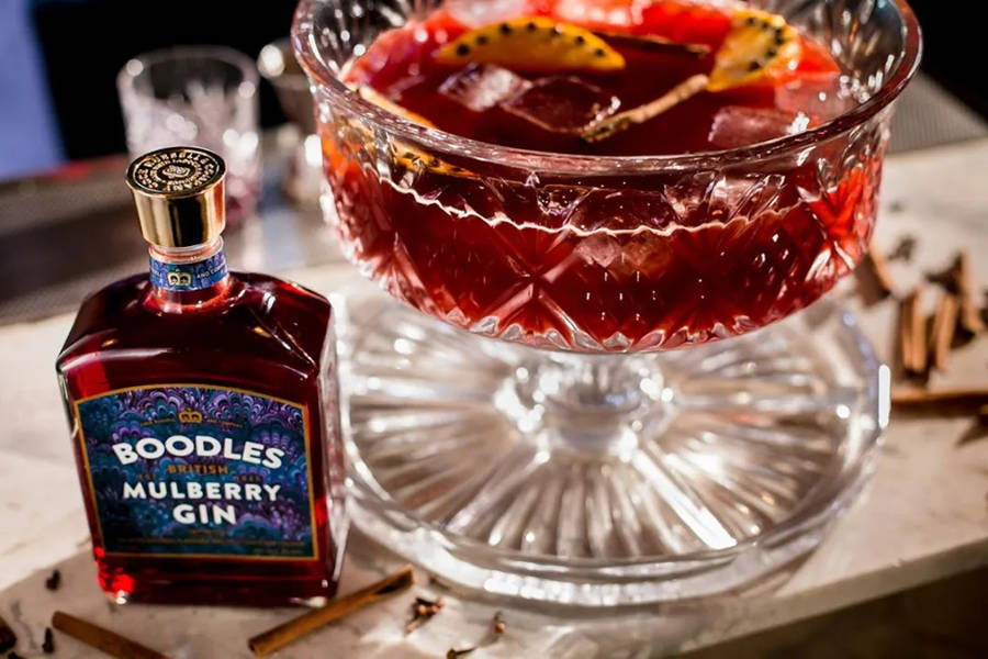 En flaska Boodles mullbärsgin bredvid en garnerad cocktail i ett kristallglas. — Mulberry bakgrund Bakgrundsbilder