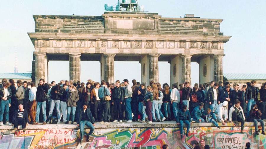 Persone che festeggiano sul Muro di Berlino con la Porta di Brandeburgo sullo sfondo. — Muro di Berlino Sfondi