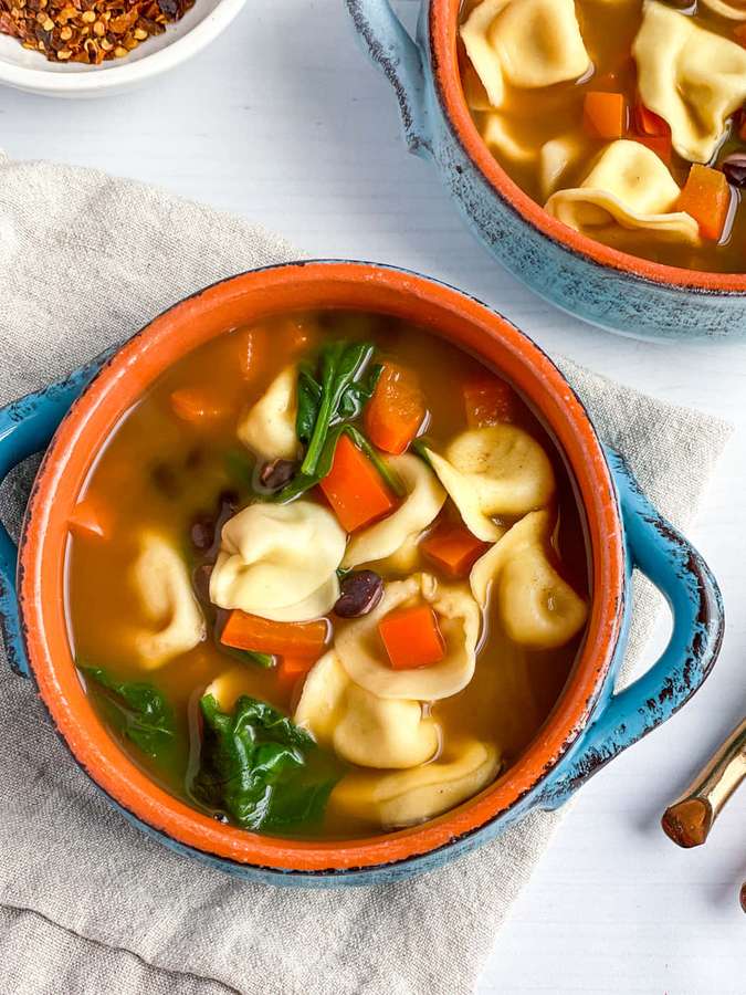 Runsas tortellinikeitto porkkanoilla, pinaatilla ja mustilla papuilla rustic sinisessä kulhossa. — Mustapapukeitto Taustakuvat