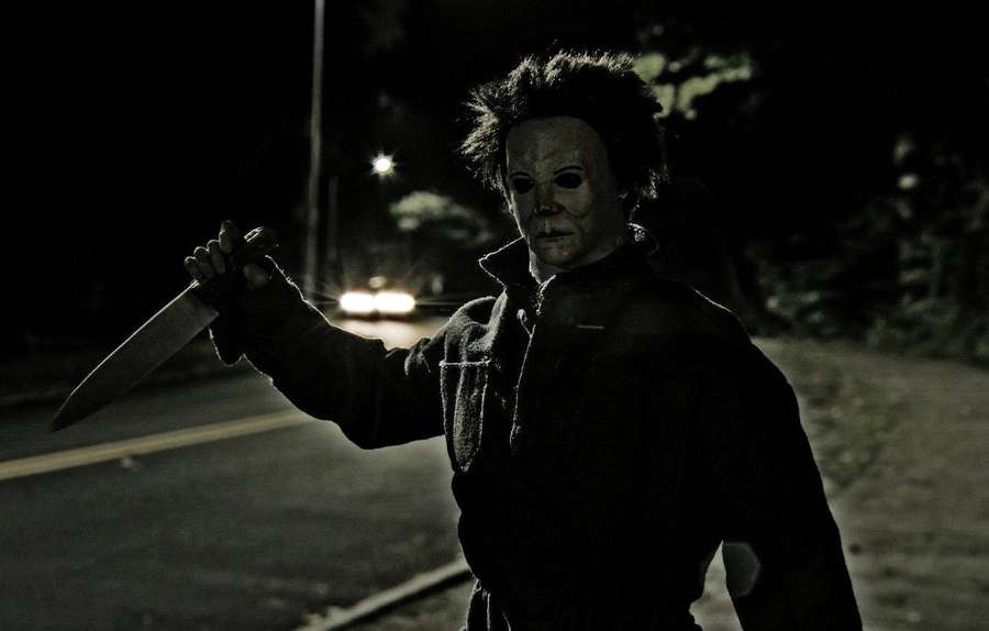 Un asesino enmascarado sosteniendo un cuchillo en una carretera oscura por la noche. — Myers Fondos de pantalla