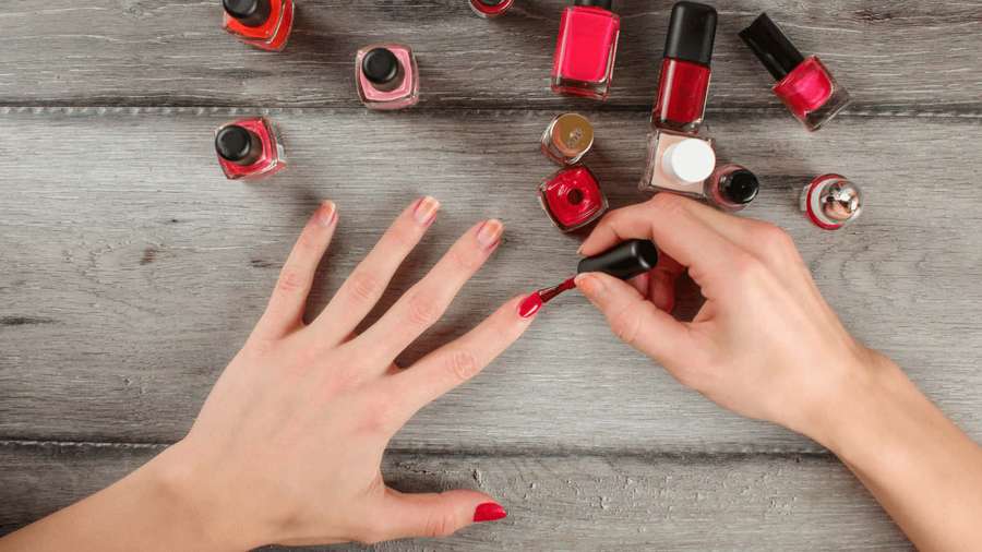Hands painting nails with red polish on a wooden table with polish bottles around. — Nail Wallpaper