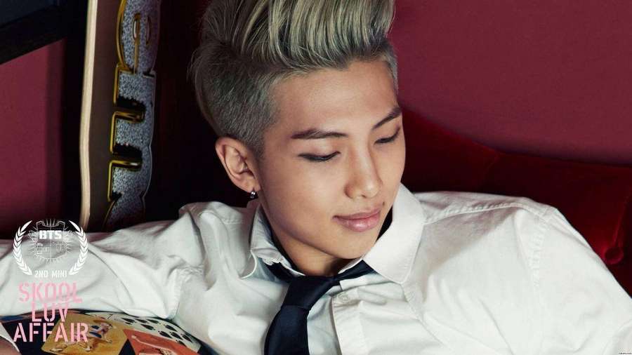 Young man with styled hair wearing white shirt and black tie resting head on red cushion. — Namjoon Background