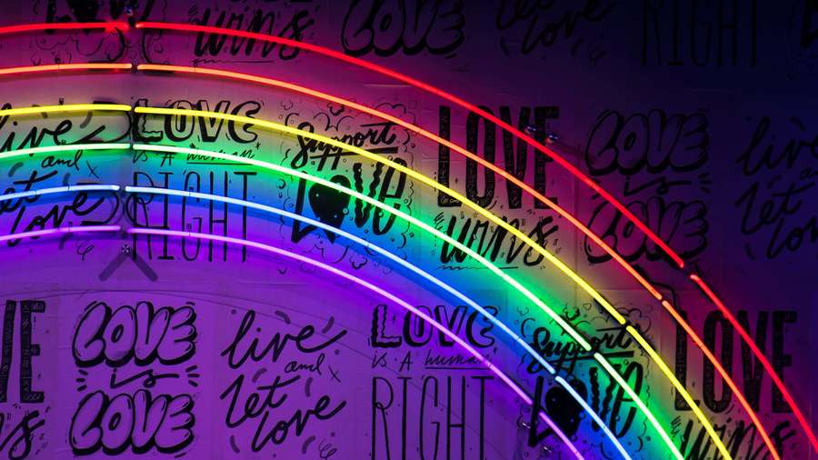 Rainbow neon lights curve over a wall with handwritten love messages. — Neon Aesthetic Background
