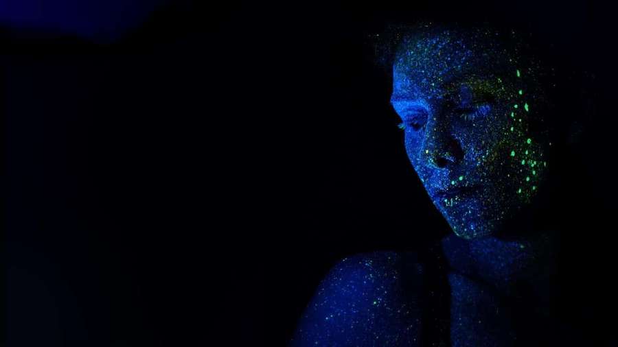 Person med lysende blått og grønt glitter på ansikt og skuldre i mørkt rom. — Neon Lyn Bakgrunner