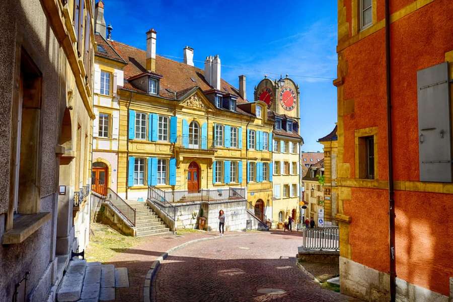 Colorful historic buildings line a cobblestone street under a bright blue sky. — Neuchâtel Wallpaper