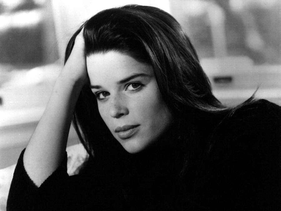 A woman with dark hair looks thoughtfully at the camera with her hand resting on her head. — Neve Campbell Wallpaper