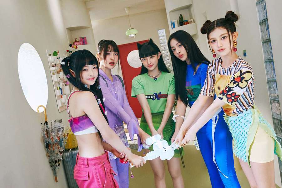 Five young women in colorful outfits holding a plush toy in a modern room. — Newjeans Wallpaper