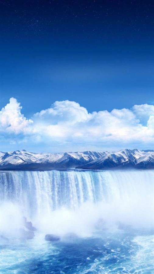 Snowcapped mountains overlook a powerful waterfall under a bright blue sky with clouds. — Niagara Wallpaper