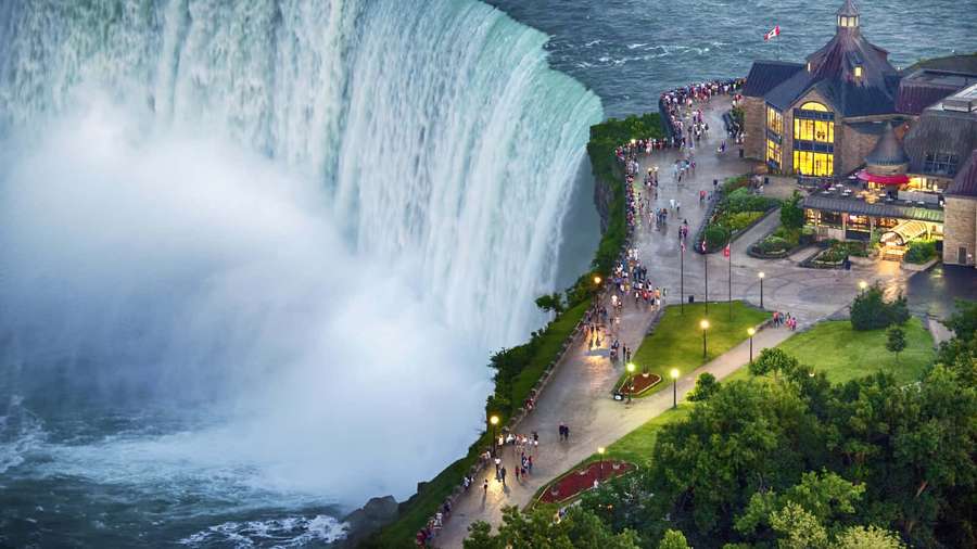 Niagara Falls at dusk with illuminated walkways and visitors near a stone building. — Niagara Falls Canada Wallpaper