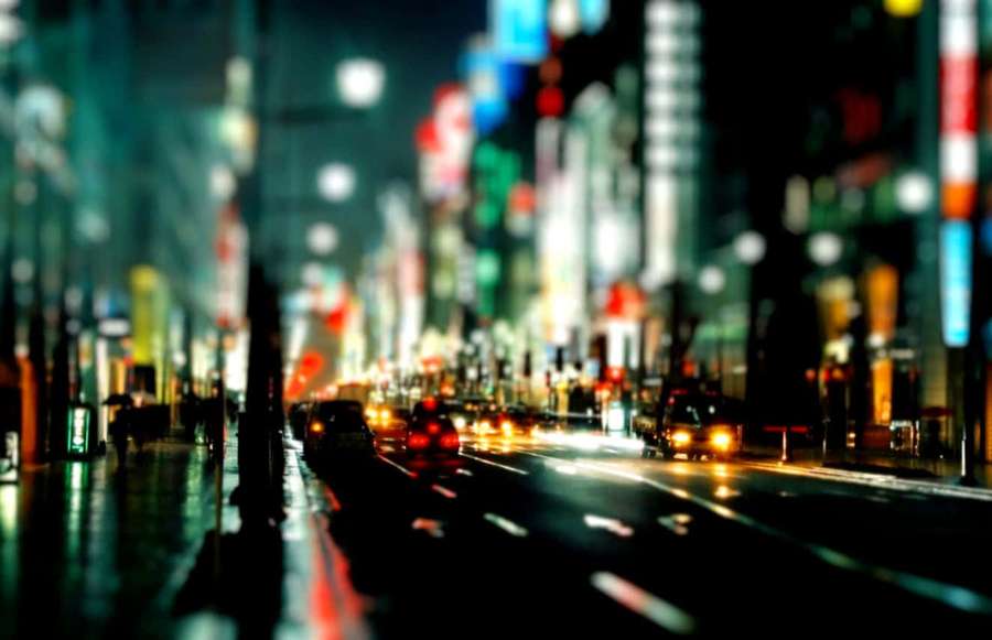 Rainy night city street with blurred neon lights and moving car headlights. — Night City Background
