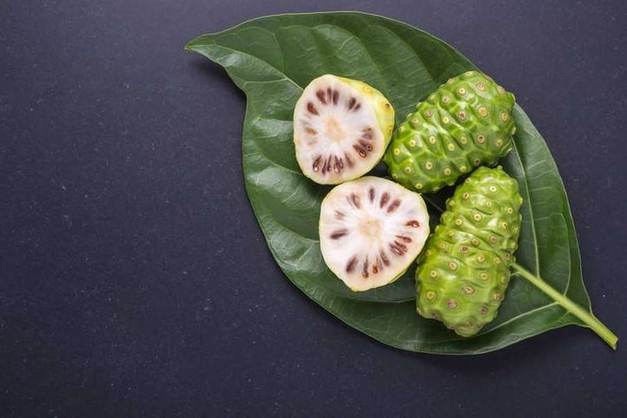 Noni affettati e interi su una foglia verde su sfondo scuro. — Noni Sfondi