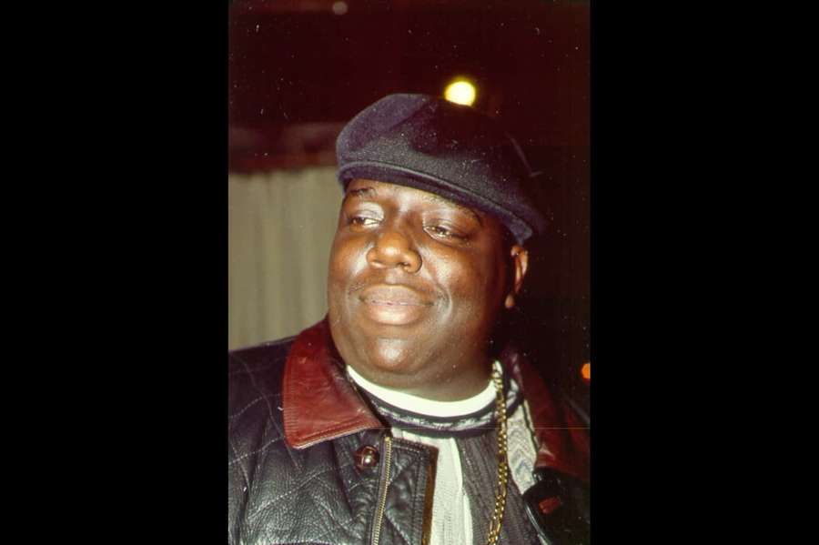 Ein lächelnder Mann mit Kappe und Lederjacke in einer schwach beleuchteten Umgebung. — Notorious Big Wallpaper