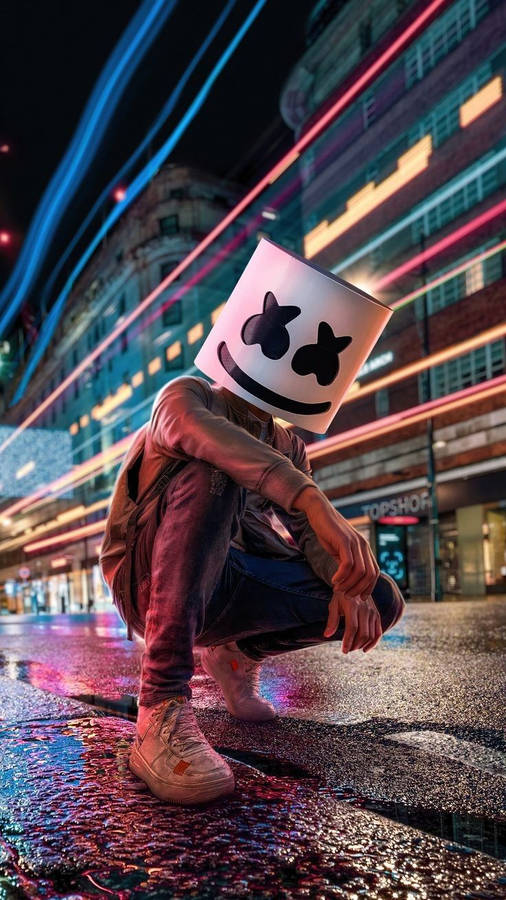 Persona con maschera marshmello accovacciata su strada bagnata della città di notte con luci al neon. — Notte Sfondi