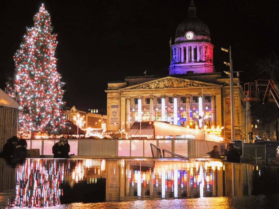 Festive Christmas tree and historic building illuminated at night with reflections in wet pavement. — Nottingham Wallpaper
