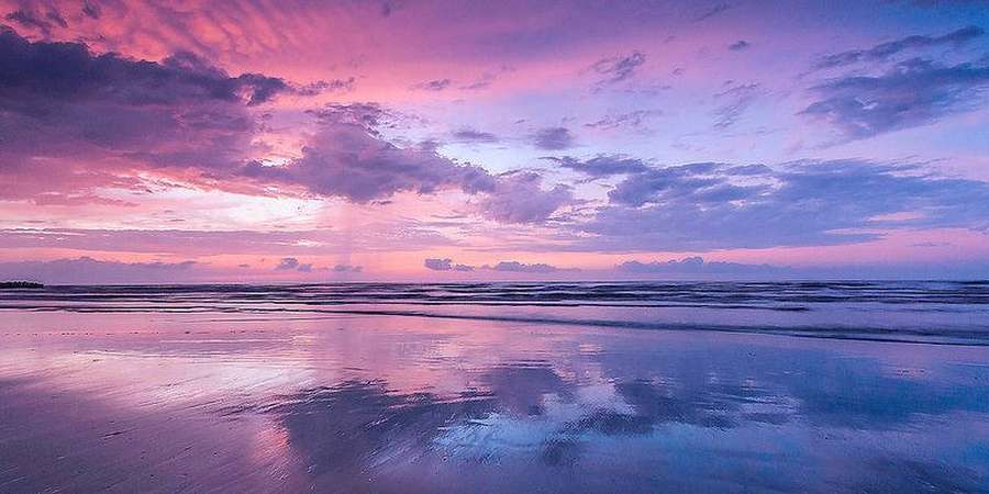 Nuvens rosa, roxas e azuis do pôr do sol refletidas na areia molhada da praia e nas ondas do oceano. — Nuvens Papéis de Parede