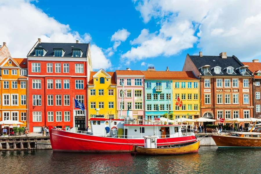 Colorful canal houses with boats docked in a sunny European city. — Nyhavn Wallpaper
