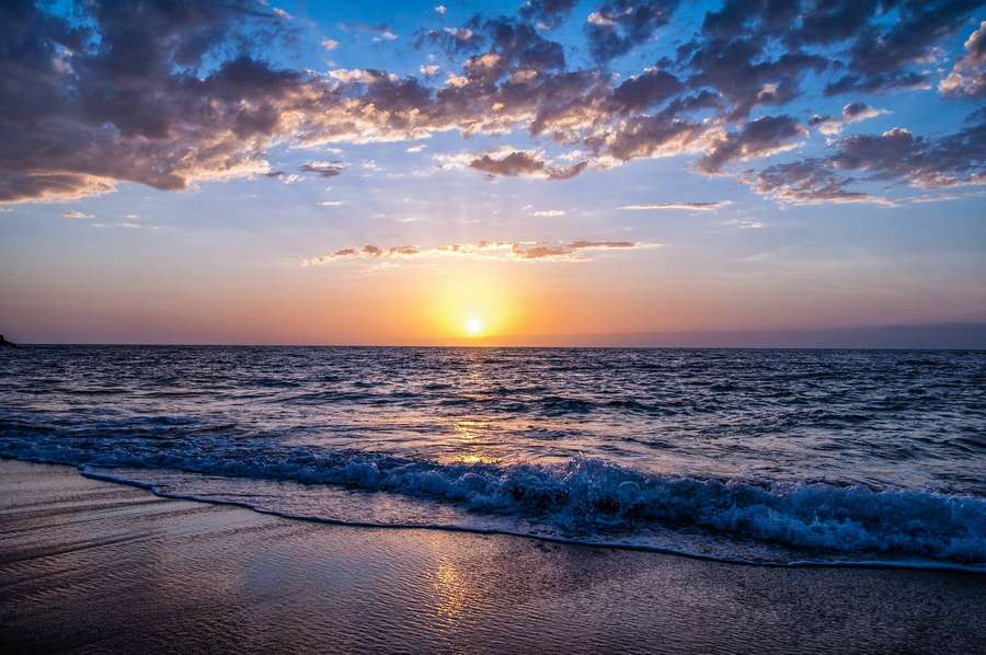 Sunset over ocean with waves washing onto wet sand under colorful clouds. — Ocean Desktop Background